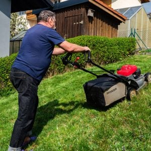 A man mowing the lawn in his yard with a Honda HRX76 lawn mower.